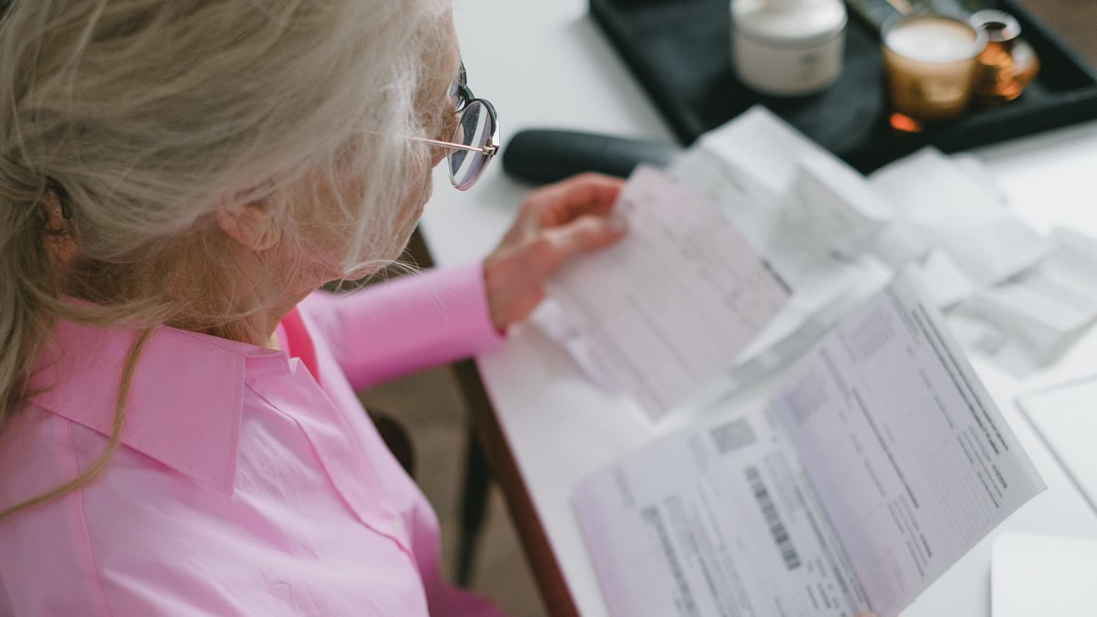 Femme âgée aux cheveux gris relisant attentivement des documents à une table, des lunettes sur le nez